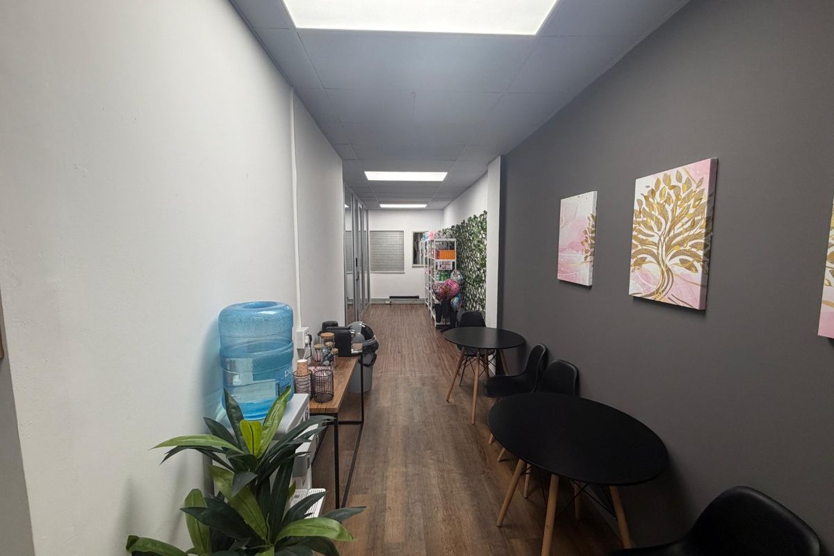 A well-lit commercial hallway featuring laminate flooring, a dark grey accent wall, and recessed ceiling panels, providing a clean and professional transition space.