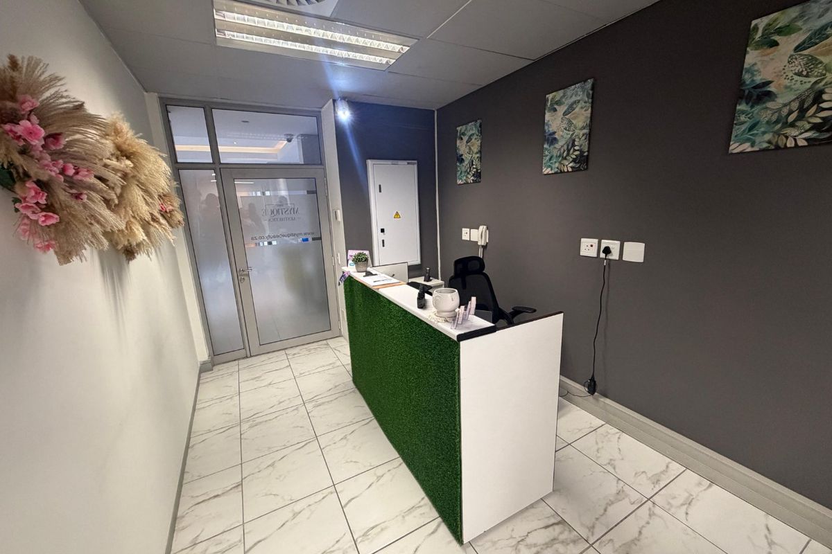 Commercial reception area featuring a built-in desk, tiled flooring, glass entrance door, and recessed ceiling lighting.