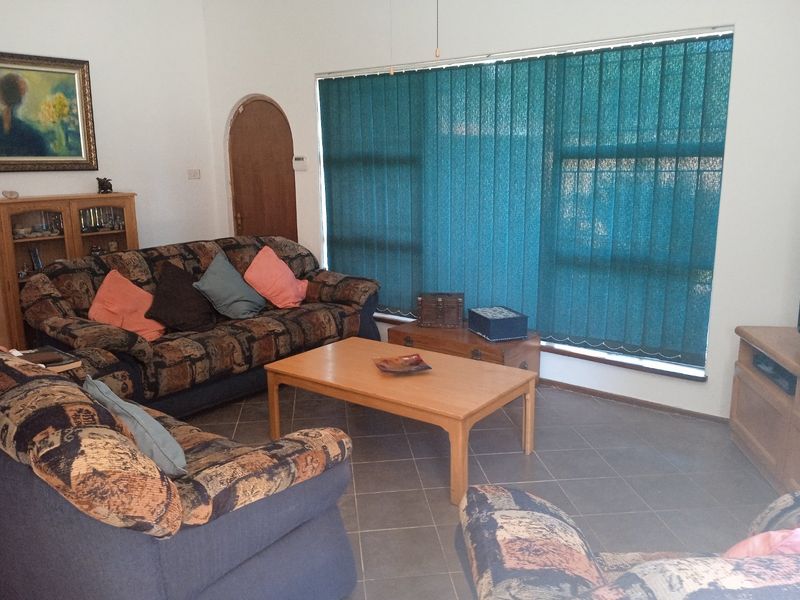 A living room featuring tiled flooring, an arched doorway, and large windows fitted with vertical blinds.