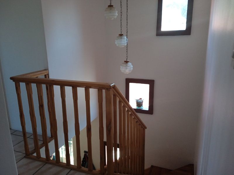 A staircase landing area featuring a wooden balustrade, tiled flooring, and a multi-tiered pendant light fixture.