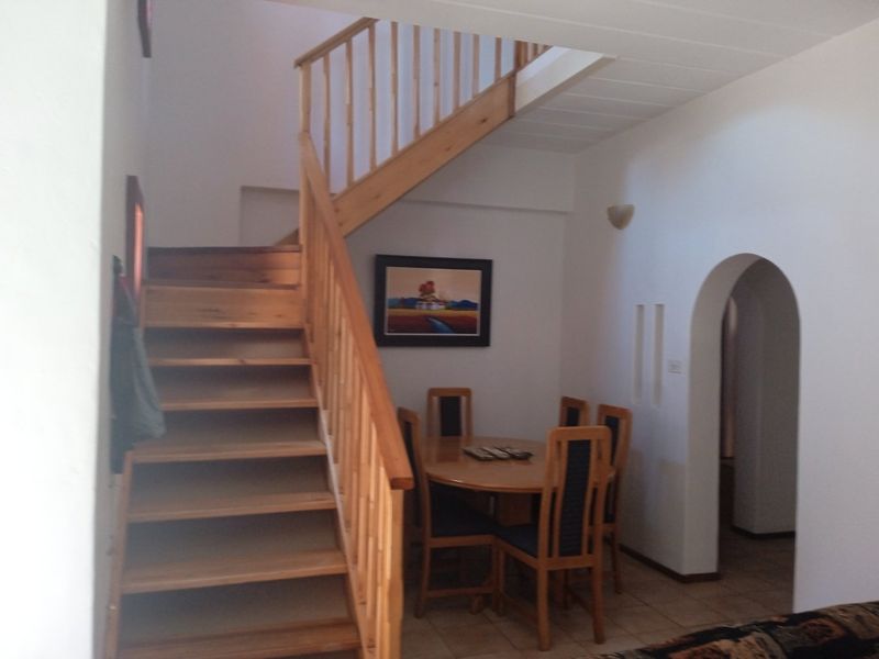 A living area featuring a wooden staircase with a balustrade, tiled flooring, and an arched doorway leading to an adjacent space.