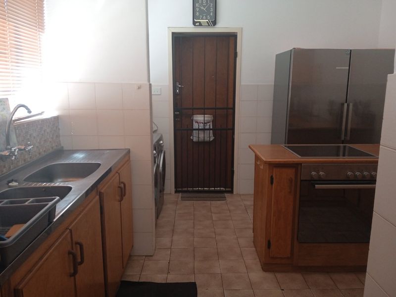 Functional kitchen featuring wooden cabinetry, a double stainless steel sink, built-in oven with electric hob, and tiled flooring with direct access to a security gate.