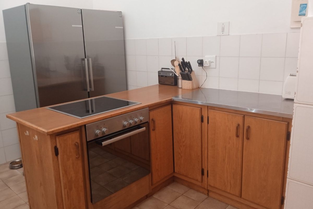 A functional kitchen featuring wooden cabinetry, a built-in oven with an electric hob, stainless steel countertops, and a tiled backsplash.