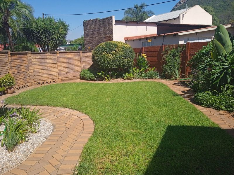 A well-maintained private garden featuring a manicured lawn, paved pathways, and established perimeter brick boundary walls.