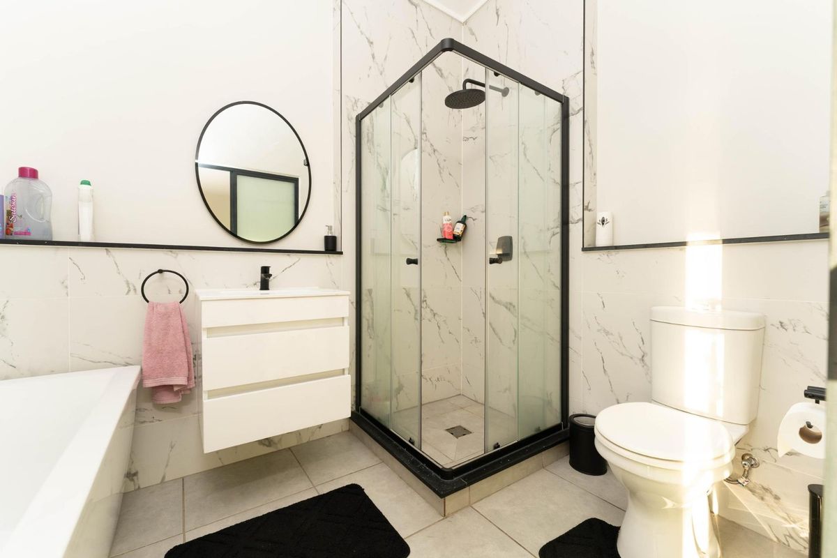 Modern bathroom featuring a corner shower enclosure, wall-mounted vanity, bathtub, and elegant marble-look wall tiling.