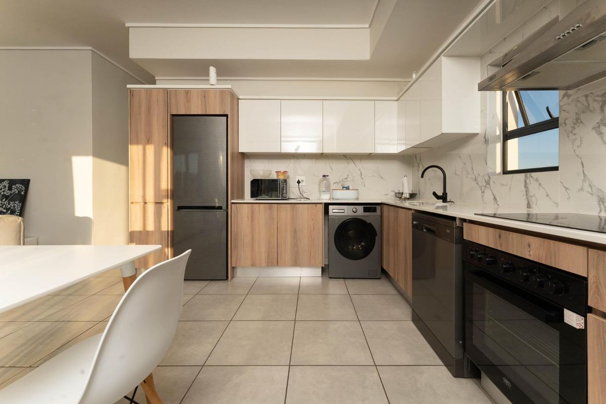 Modern kitchen featuring sleek wood-tone and white cabinetry, marble-look splashback, high-quality built-in appliances, and neutral tiled flooring.