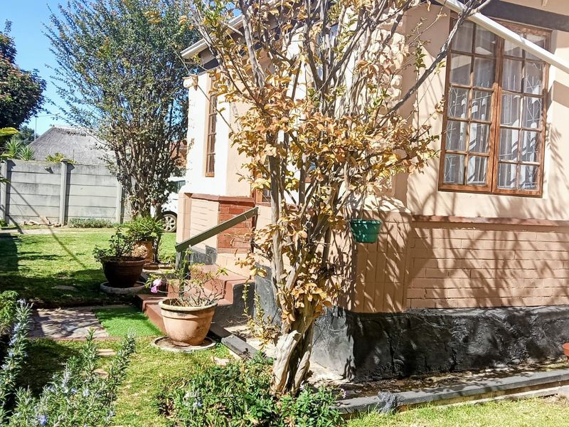 Rear exterior view of the property featuring a brick facade, timber-framed windows, and a surrounding garden area with a concrete boundary wall.