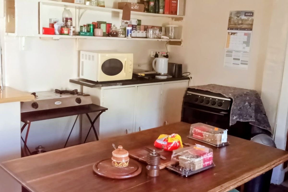 A functional kitchen area featuring basic base cabinetry, open wall shelving, and a freestanding oven, requiring cosmetic updates to modernize the space.