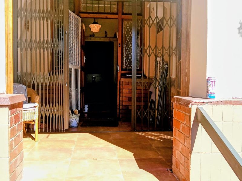 A covered front entrance porch featuring tiled flooring, brick pillars, and a metal security gate leading into the home.