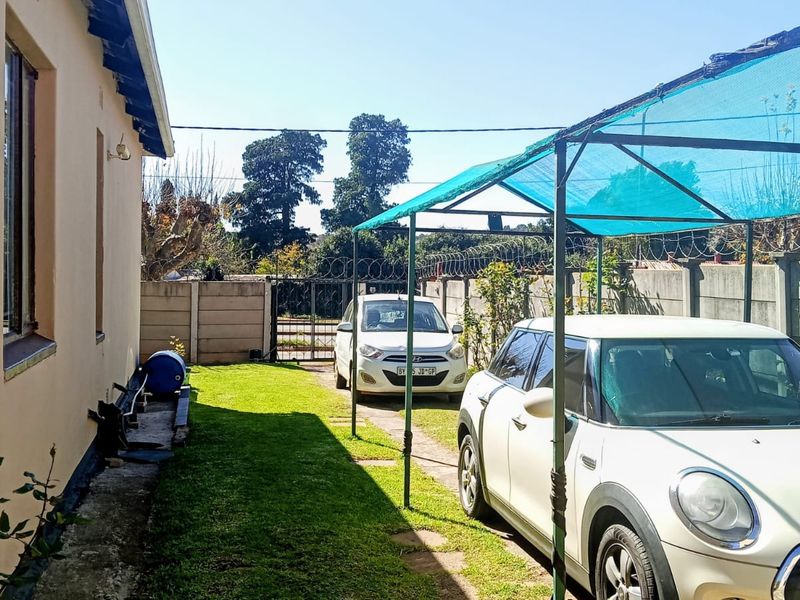 Rear exterior area featuring a lawn, precast concrete boundary wall with security fencing, and a shade cloth carport structure.