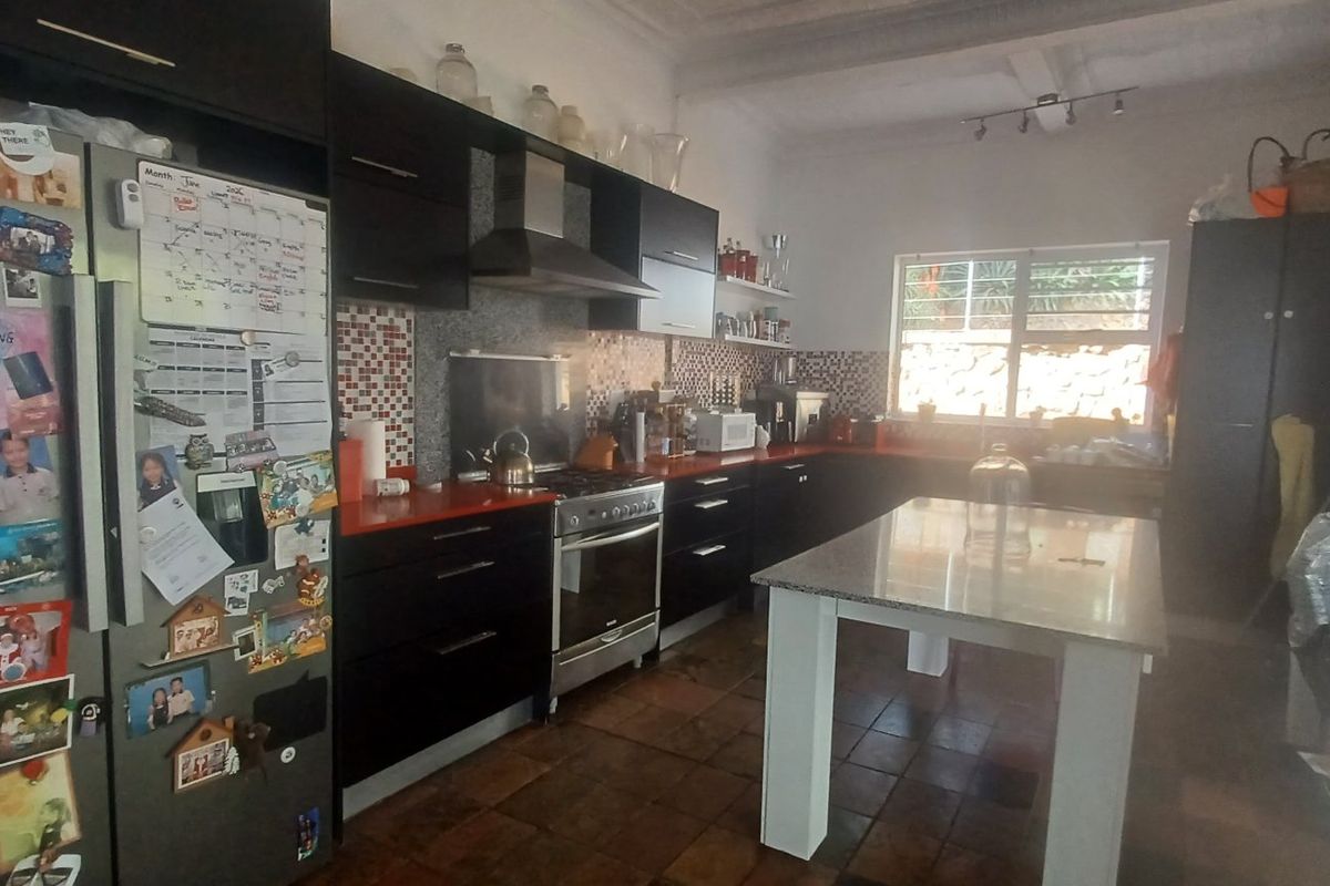 A functional kitchen featuring dark cabinetry, a central island, gas stove with extractor, and tiled flooring, with direct access to an outdoor area.
