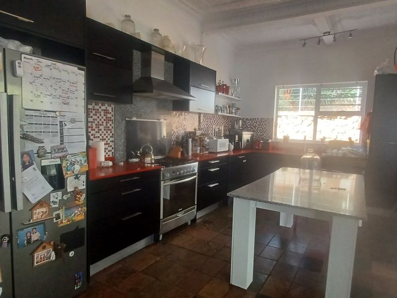 A functional kitchen featuring dark cabinetry, a central island, gas stove with extractor, and tiled flooring, with direct access to an outdoor area.
