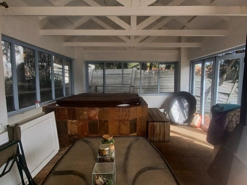 Enclosed patio area featuring a built-in hot tub, exposed timber ceiling beams, and a fireplace, offering a versatile space for relaxation and entertainment.