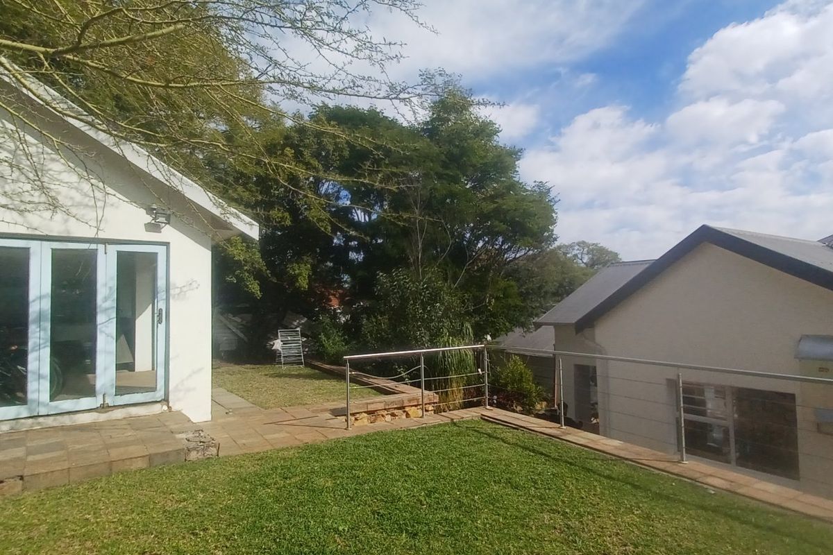 Rear view of the property featuring a paved patio area, lawn, stainless steel balustrade, and bi-fold doors leading into the home.