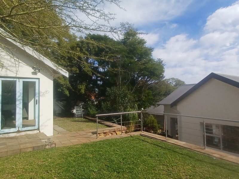 Rear view of the property featuring a paved patio area, lawn, stainless steel balustrade, and bi-fold doors leading into the home.