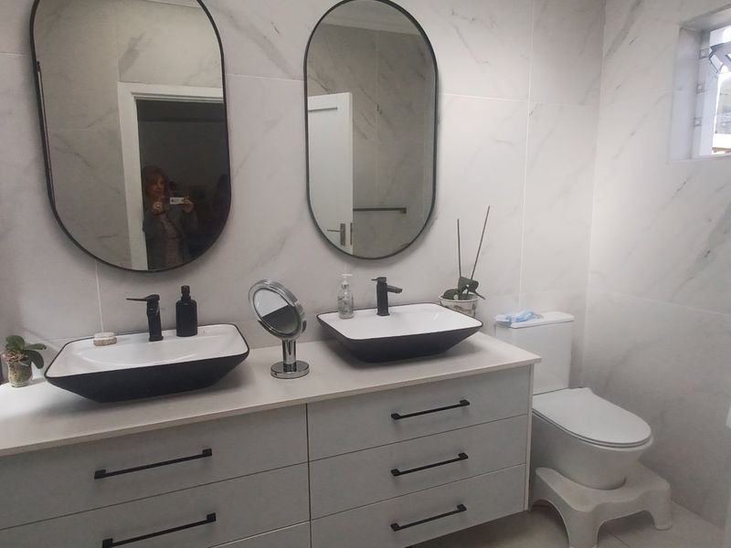 Modern bathroom featuring a double vanity with vessel sinks, marble-look wall tiles, and a walk-in shower with a built-in niche.