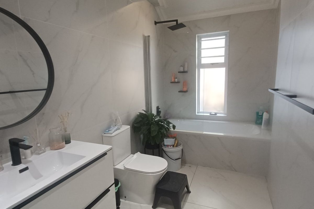 Modern bathroom featuring marble-look wall tiles, a sleek vanity with basin, a bathtub with shower head, and contemporary black fixtures.
