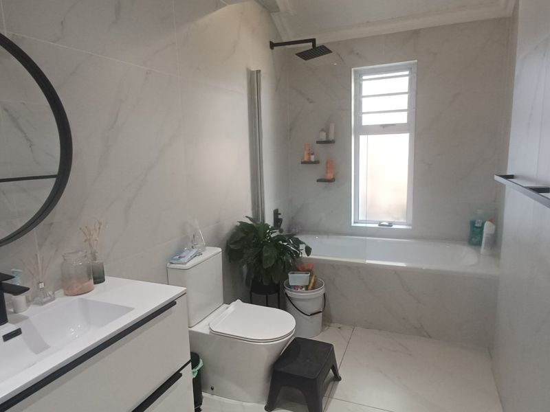 Modern bathroom featuring marble-look wall tiles, a sleek vanity with basin, a bathtub with shower head, and contemporary black fixtures.
