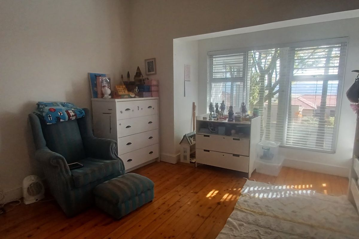 A bedroom featuring warm timber flooring and a large window with venetian blinds, providing natural light and a view of the exterior.