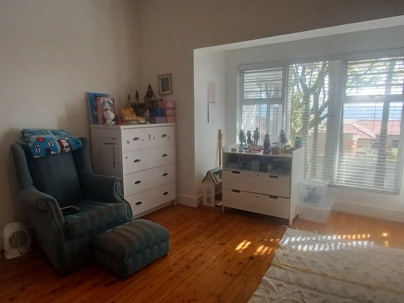 A bedroom featuring warm timber flooring and a large window with venetian blinds, providing natural light and a view of the exterior.