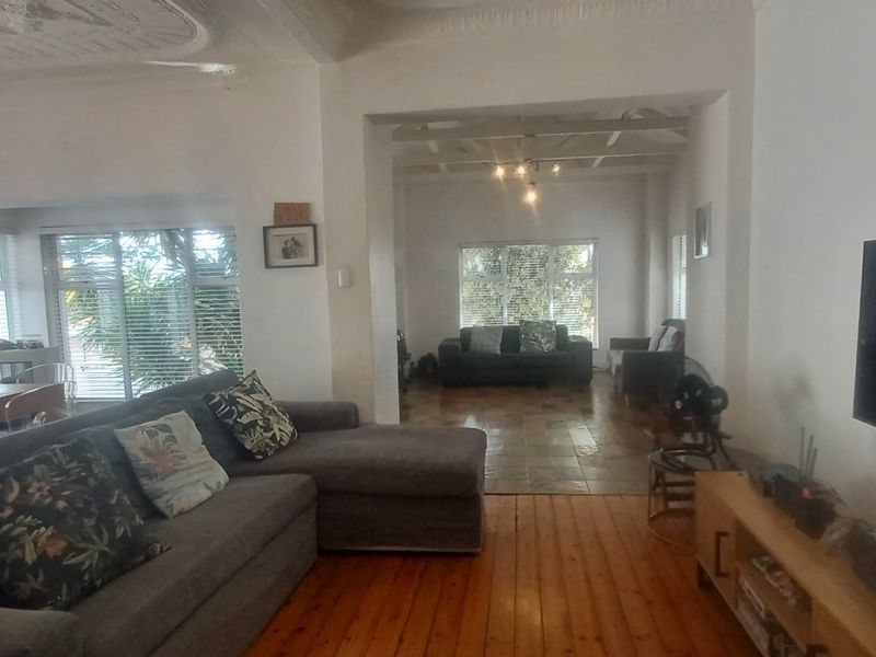 Spacious open-plan living area featuring a blend of hardwood and tiled flooring, ornate ceiling detailing, and exposed beams, creating a bright and versatile living space.