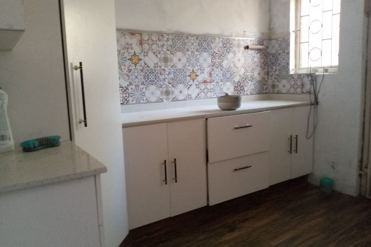 A compact kitchen area featuring white cabinetry, stone countertops, and a decorative tile backsplash, currently requiring finishing touches to the walls and electrical fixtures.