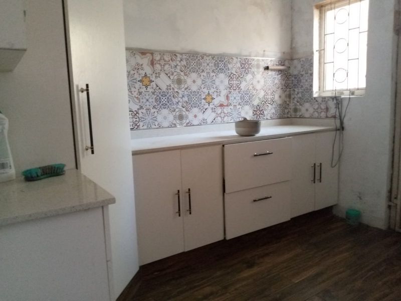 A compact kitchen area featuring white cabinetry, stone countertops, and a decorative tile backsplash, currently requiring finishing touches to the walls and electrical fixtures.