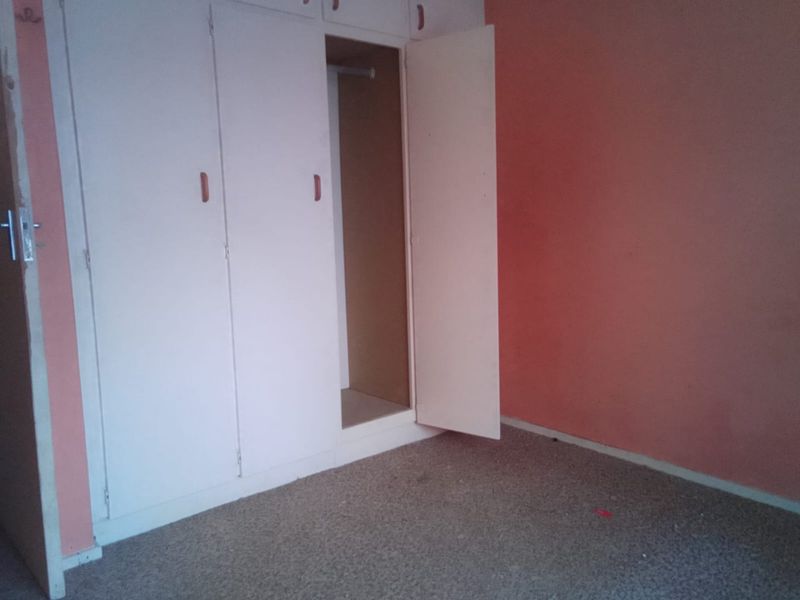 A vacant bedroom featuring built-in cupboards and carpeted flooring, requiring cosmetic updates to refresh the space.