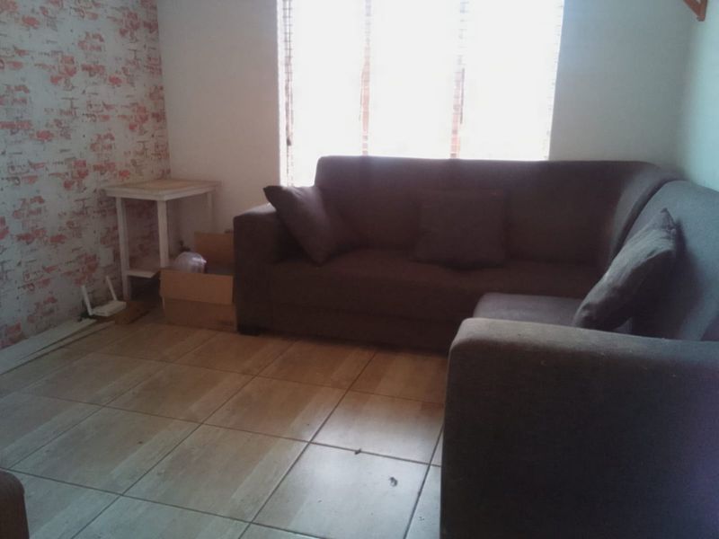 A living room area featuring tiled flooring and window blinds, providing a functional space for relaxation.