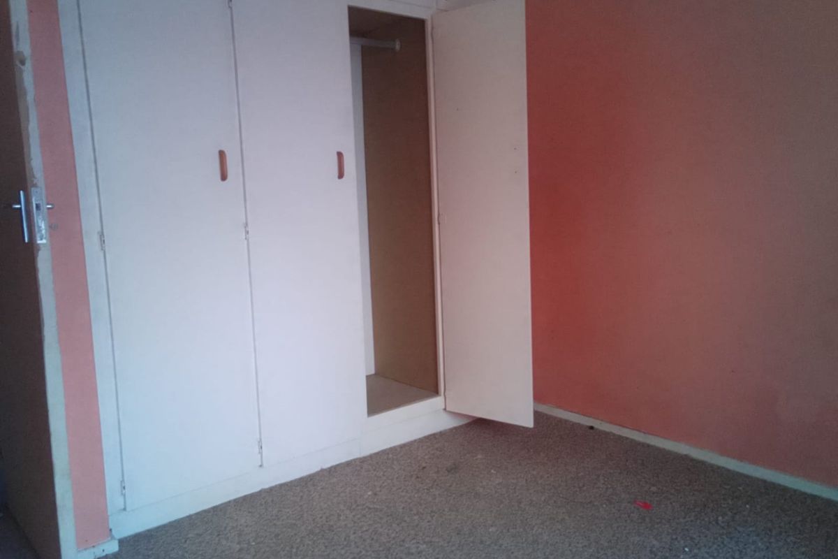 An empty bedroom featuring built-in cupboards, requiring cosmetic updates to the wall finishes and flooring to improve its overall appeal.