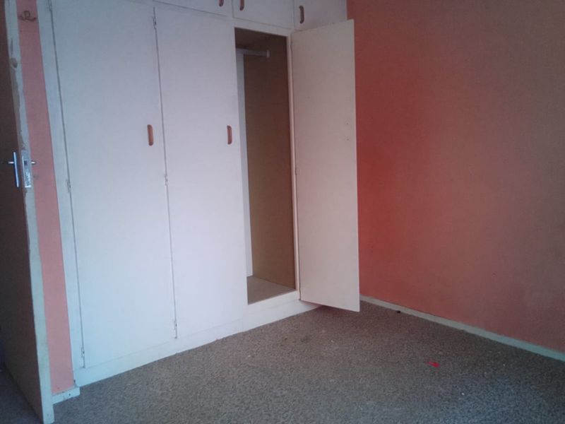 An empty bedroom featuring built-in cupboards, requiring cosmetic updates to the wall finishes and flooring to improve its overall appeal.