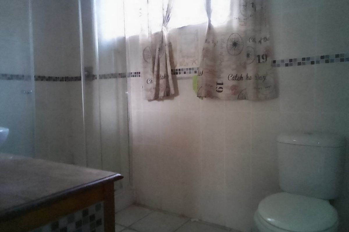 A dated bathroom featuring a shower enclosure, toilet, and vanity cabinet with tiled finishes throughout.