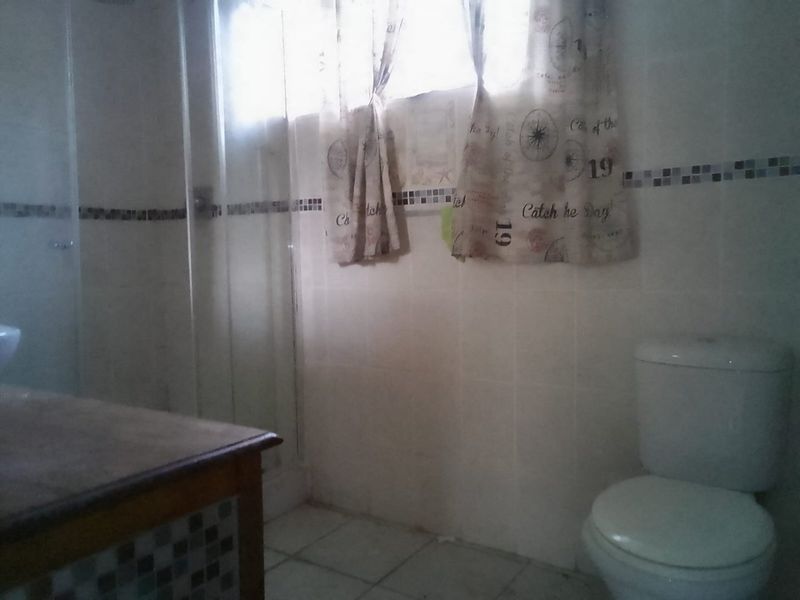 A dated bathroom featuring a shower enclosure, toilet, and vanity cabinet with tiled finishes throughout.