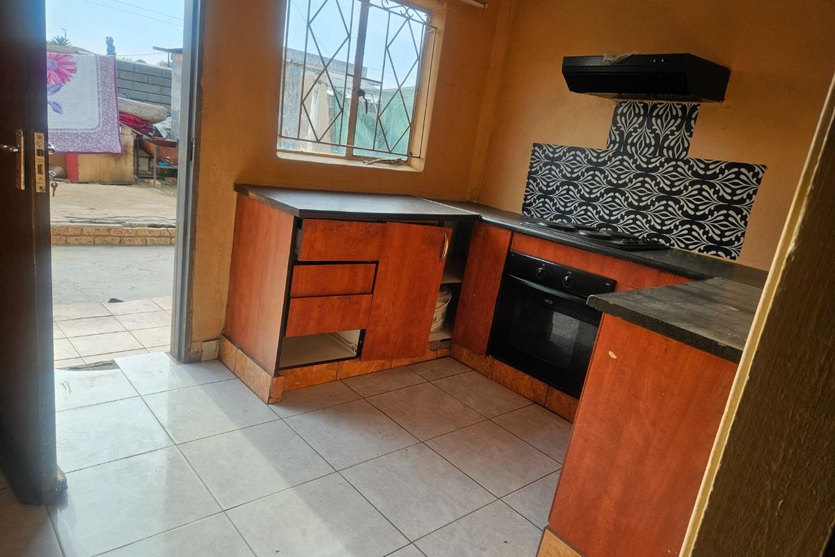 A compact kitchen featuring built-in cabinetry, an integrated oven, and extractor fan, with direct access to the exterior area.