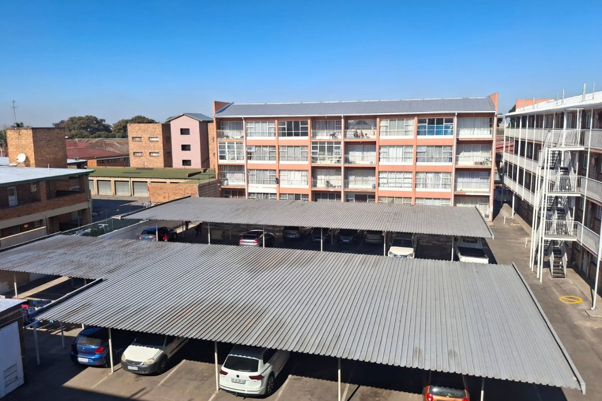 An elevated view of a residential apartment complex featuring a large paved parking area with covered carports and external building access.