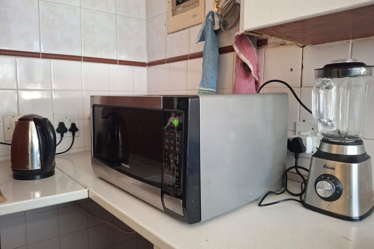 A dated kitchen corner featuring tiled backsplashes, laminate countertops, and an exposed electrical distribution board, showing signs of wear and aging.