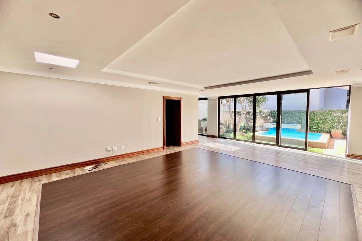 Spacious, empty living area featuring recessed ceiling detail, modern laminate flooring, and large sliding glass doors providing direct access to the pool area.