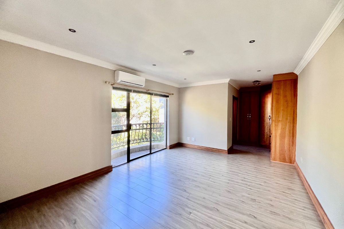 Spacious bedroom featuring light laminate flooring, built-in wooden cupboards, an air conditioning unit, and a sliding door leading to a private balcony.