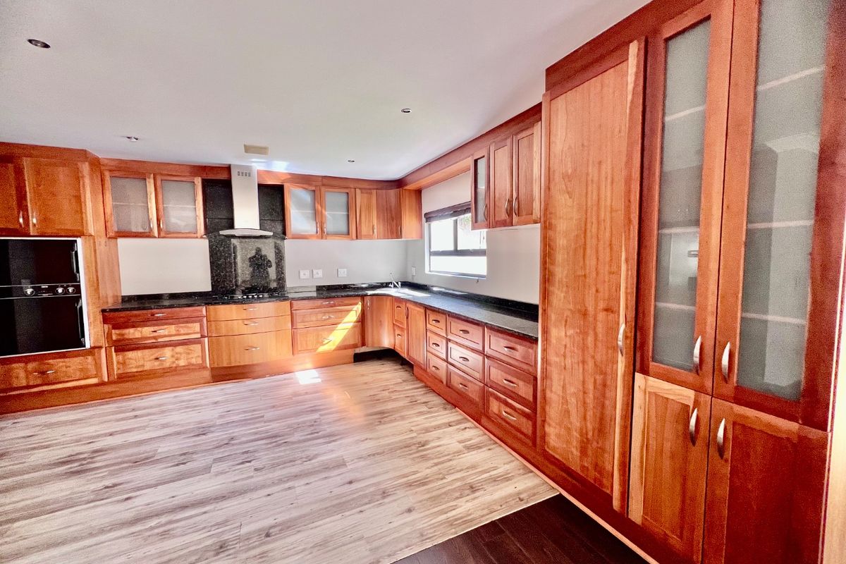 Spacious kitchen featuring extensive wooden cabinetry, granite countertops, built-in oven, extractor fan, and modern wood-look flooring.