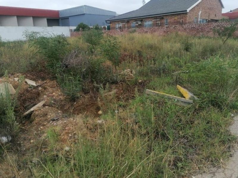 A vacant residential plot featuring overgrown vegetation and debris, situated in a developed neighborhood with existing boundary walls.