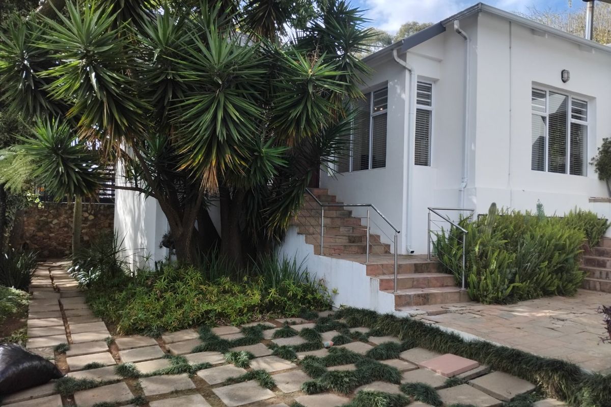 Rear exterior view featuring a white facade, tiled staircase with stainless steel handrails, and a paved garden path surrounded by established greenery.