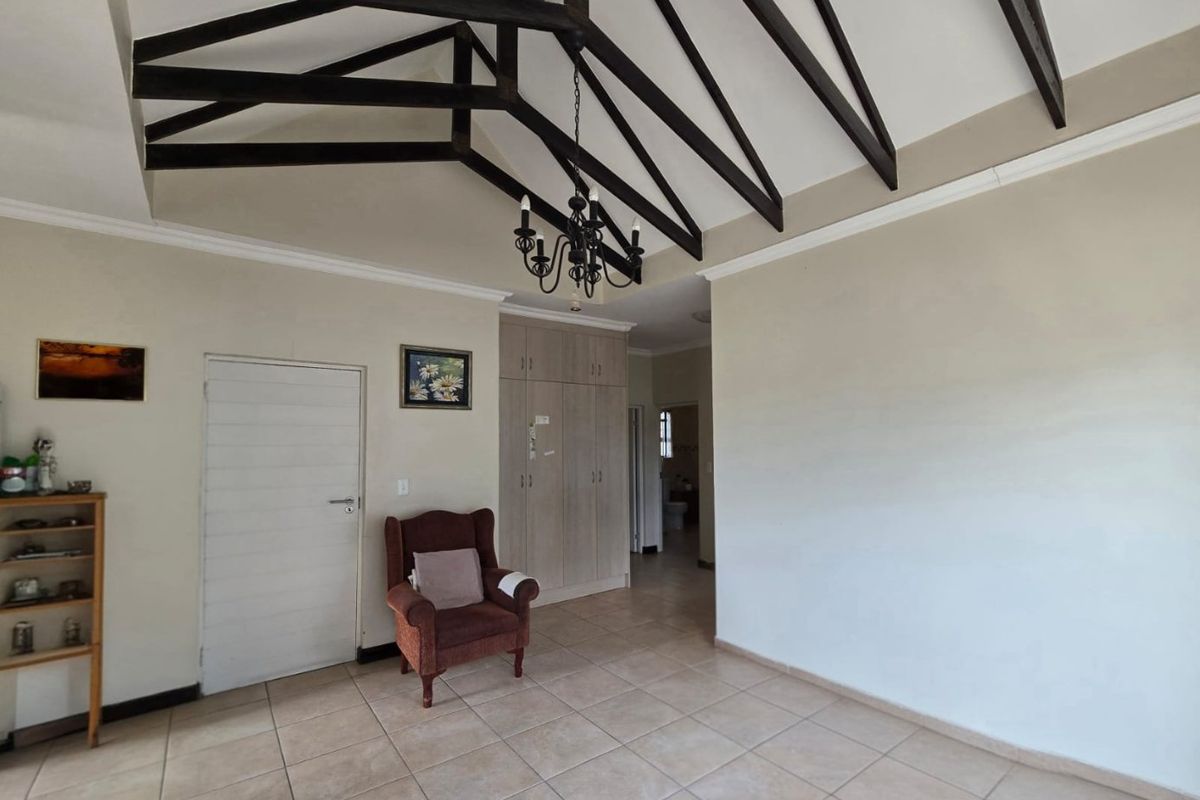 Spacious living area featuring a vaulted ceiling with exposed timber beams, tiled flooring, and built-in storage cupboards.