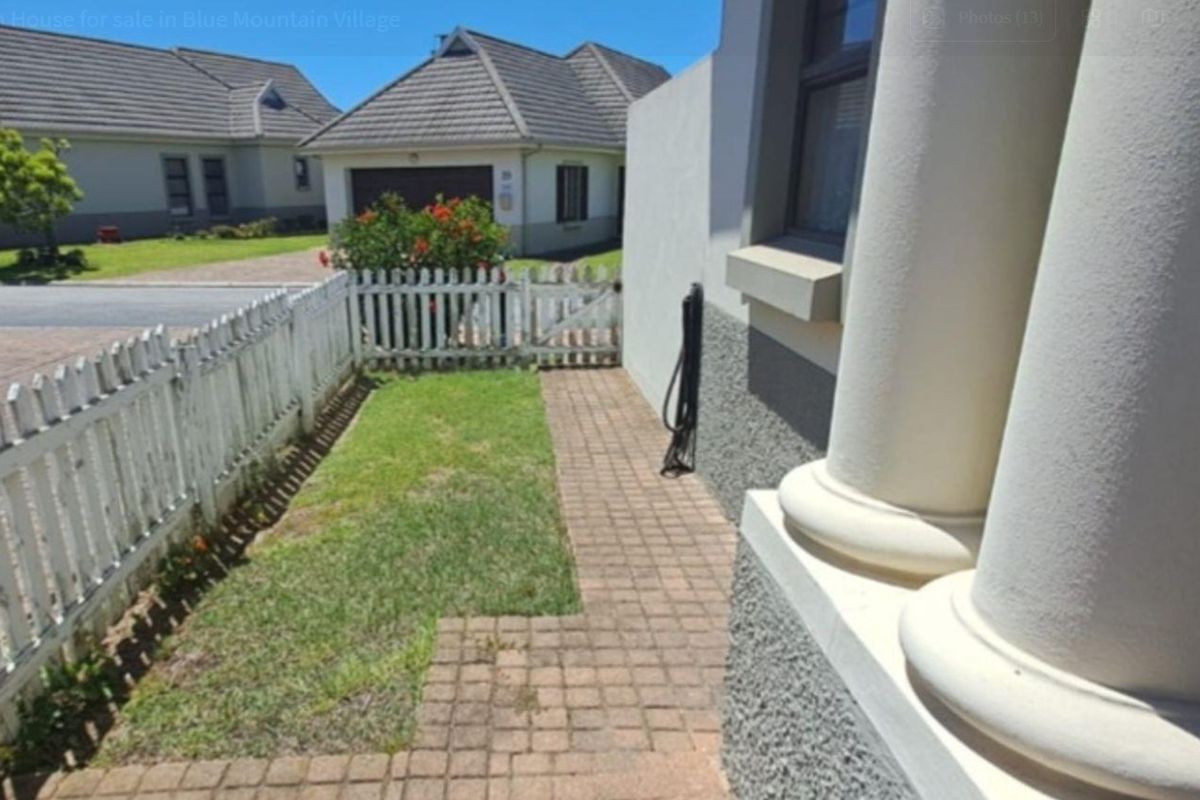 A side garden path featuring a paved walkway, white picket fencing, and decorative architectural columns along the exterior wall.