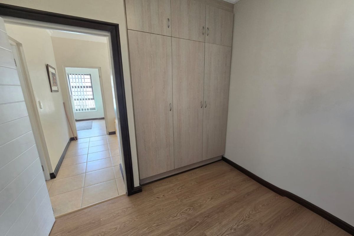 A clean, empty bedroom featuring light wood-look laminate flooring and built-in cupboards, with a view into the adjacent tiled hallway.