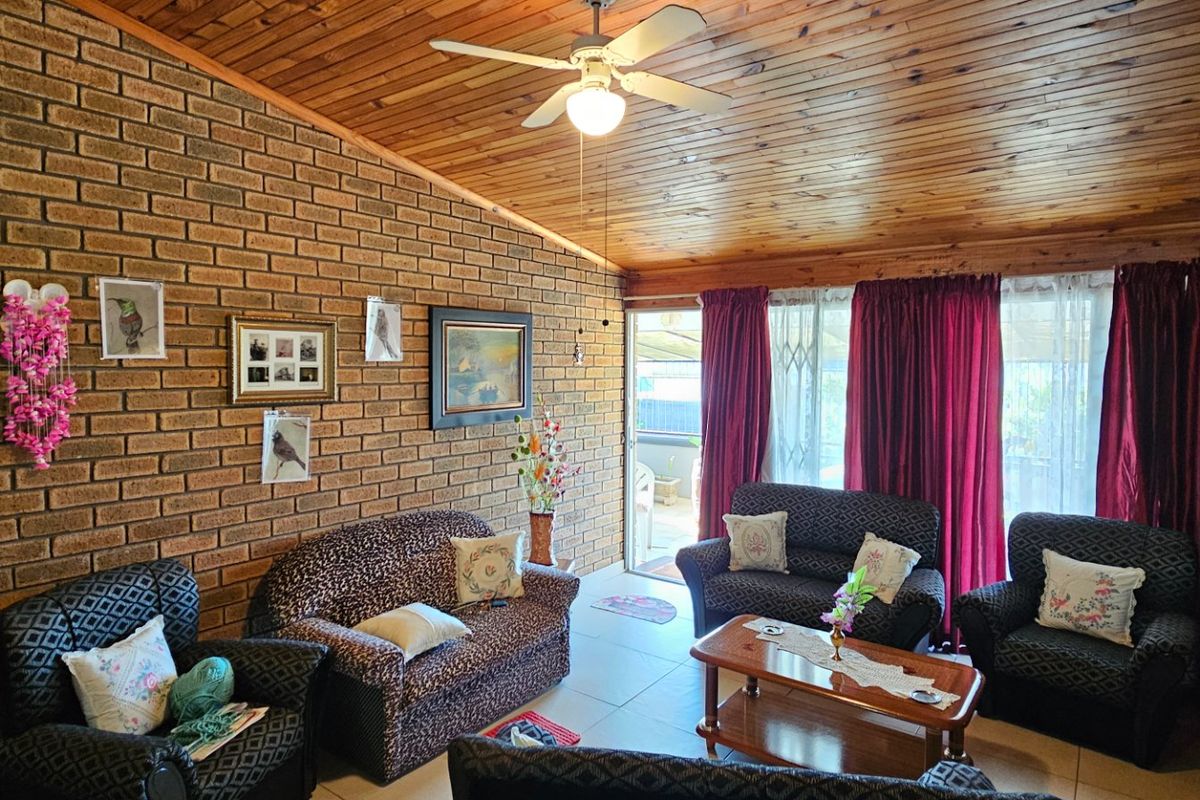 Spacious living room featuring a vaulted timber ceiling, exposed brick feature wall, tiled flooring, and direct access to the outdoor area via sliding doors.