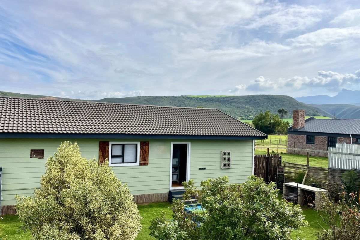 Rear view of a green timber-clad house featuring a tiled roof, built-in outdoor braai area, and scenic mountain views.