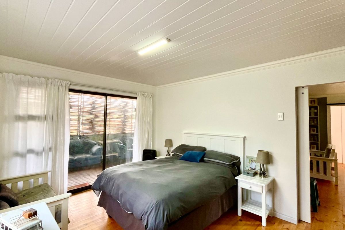A bright bedroom featuring timber flooring, a tongue and groove ceiling, and a sliding glass door providing access to an outdoor area.