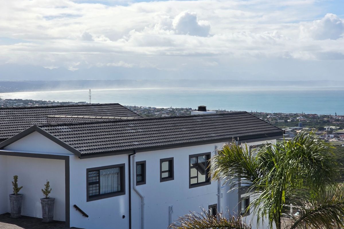 Rear view of the property featuring a tiled roof, modern aluminium window frames, and an expansive coastal landscape view.