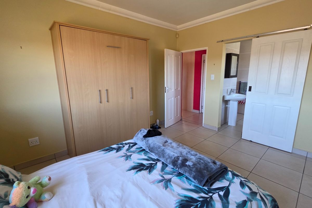 Bedroom featuring tiled flooring, built-in wardrobe, and an en-suite bathroom with a pedestal basin accessed via a sliding door.