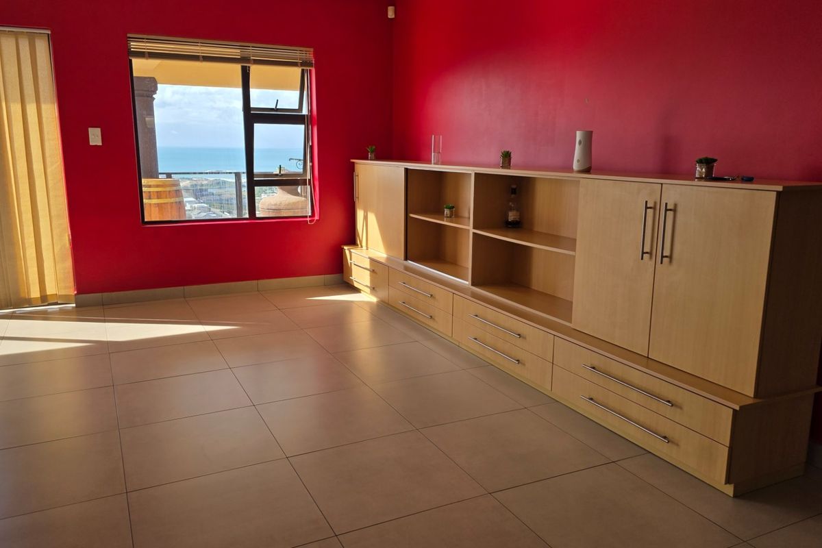 Spacious living area featuring large built-in cabinetry, neutral tiled flooring, and a sliding door leading to a balcony with ocean views.